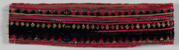 E/10999/ML - Pas męski szyty maszynowo z grubego lnianego płótna. Obszyty szczoteczką w kolorze czerwonym oraz cienką wełną w kolorze amarantowym i taśmą srebrzystą. Na środek naszyty jest czarny aksamit wycięty „w okienka” – ażurowy szlak z rombów. Pod okienka podłożone taśmy biało-czerwono-zielone ze srebrna nitką oraz amarantowe i zielone. Zapinany na 3 ciemne guziki i pętelki ręcznie wykonane z nici. 