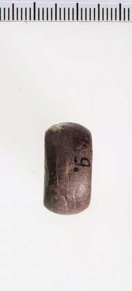 wykonany z łupka owruckiego; kształtu płaskiego walca, bardzo łagodnie półokrągło profilowanego; przy otworze płasko ścięty; otwór dość szeroki, cylindryczny