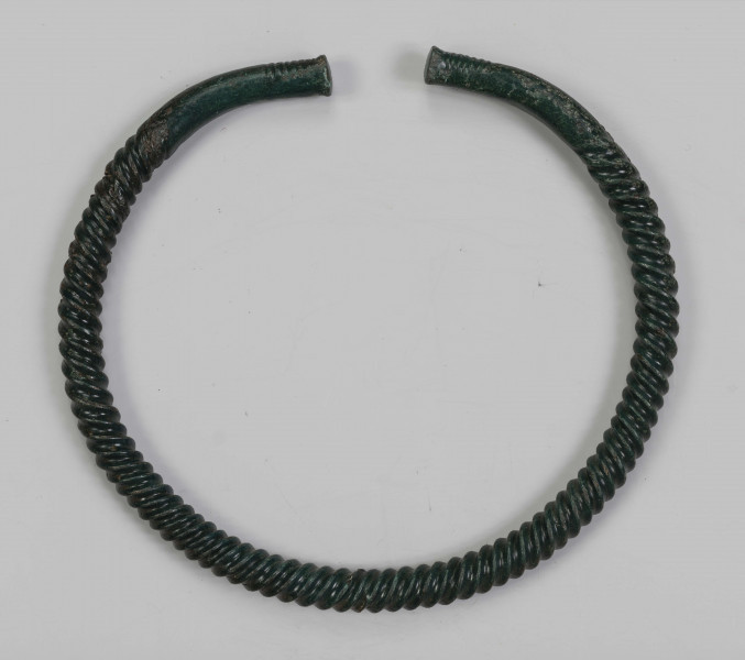 1395/A/ML/2 - Naszyjnik brązowy wykonany z pręta lanego, pokrytego zieloną patyną. Całość spiralnie skręcona; końcówki płasko zaklepane, nieskręcane jedynie ozdobione kilkoma żłobkami nacietymi na zewnętrznej stronie naszyjnika