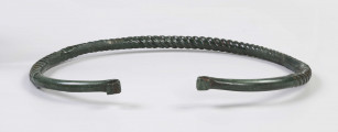 1395/A/ML/1 - Naszyjnik brązowy wykonany z brązowego pręta lanego, pokryta zieloną patyną. Całość spiralnie skręcona; końcówki rozklepane (płasko) i wywynięte na zewnątrz; końcówki naszyjnika gładkie nie skręcane 