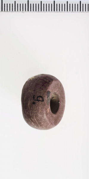 wykonany z łupka owruckiego; kształtu płaskiego walca, bardzo łagodnie półokrągło profilowanego; przy otworze płasko ścięty; otwór dość szeroki, cylindryczny