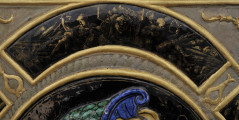 detal - emaliowana ćwiartka koła ze złoceniami na czarnym tle, słabo widoczna złota dekoracja głowy maszkarona, sylwetki męskiej i nieczytelnych dekoracji.