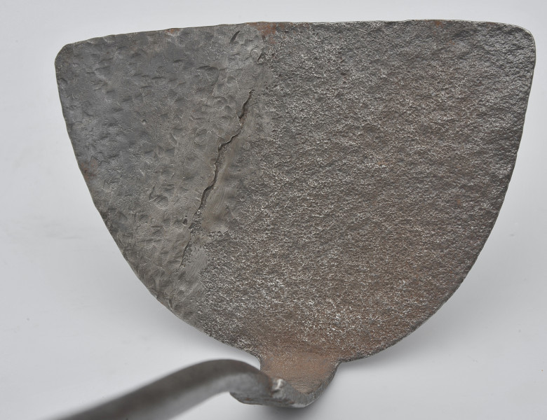 detal - łopatka. Widok półkolistego sztychu, zwróconego krawędzią do góry. Widoczne liczne wgłębienia ciemniej powierzchni oraz ślady rdzawej korozji.