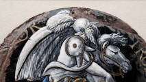awers – fragment górny, ujęcie powyżej pasa brodatego mężczyzny w hełmie zdobionym piórem i niebieskim kamieniem, łeb konia, duże uszkodzenia emalii na krawędziach.