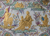 ujęcie z góry - fragment (sceny mitologiczne), pięć złotych postaci, z lewej kobieta ze sztandarem i lwem po środku kobieta siedząca z dzieckiem na kolanach po prawej postać w zbroi z niebieską tarczą, w tle po prawej zabudowania po lewej leżąca postać obok zwierzęta, kwiaty.