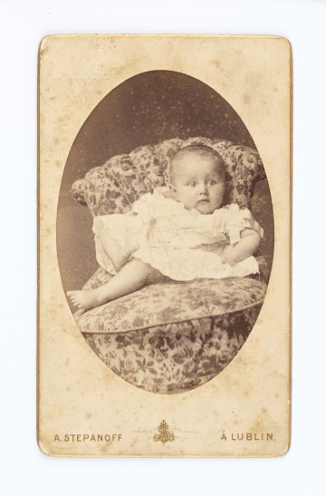 Fotografia owalna Henryki Rodkiewiczówny w wieku niemowlęcym. Siedzi na krześle ubrana w białą sukienkę.