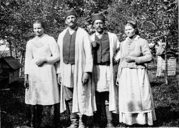 Fotografia czterech osób ubranych w strój biłgorajski pozujących na tle uli.