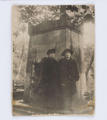 Fotografia przedstawia dwie kobiety, ubrane na czarno, stojące obok grobu Bolesława Prusa na Powązkach. Oktawia Głowacka stoi po lewej stronie, ubrana jest w czarny płaszcz, czarne rękawiczki, w prawej ręce trzyma laskę na której się opiera, a na głowie ma czarny kapelusz. Po prawej stronie stoi Emilia Kapaonowa ubrana w czarnym płaszcz z kołnierzem obszytym futrem, w prawej ręce trzyma małą, torebkę. Za plecami kobiet, znajduje się bryła grobu Bolesława Prusa w kształcie prostopadłościanu, zwieńczonego ozdobną koroną. Na drugiej stronie, w lewym, dolnym rogu znajduje się napis wykonany ołówkiem: „Pomnik B. Prusa/  na Powązkach”. Wyżej umieszczony jest prostokątny, drukowany znak wewnątrz którego widnieje napis: „LEONAR”.