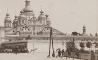 zbliżenie na mur otaczający teren klasztoru oraz ukazującą się za nim cerkiew św. Michała. W prawym rogu kadru przechodnie: mężczyźni i kobiety z parasolkami podążający w kierunkiu świątyni
