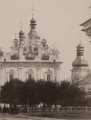 zbliżenie na lewą część elewacji Soboru Uspienskiego, zasłoniętą u dołu drzewami. Po prawej stronie soboru wieża rozebranej w 1893 roku cerkwi Świętych Piotra i Pawła zwieńczona hełmowym dachem