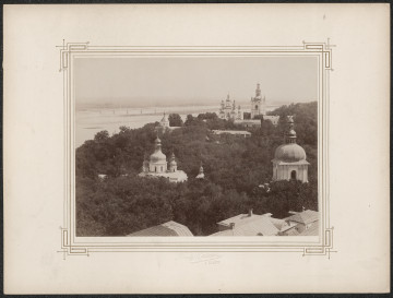 pośrodku białej karty zdjęcie z lotu ptaka na wieże i kopuły klasztoru prawosławnego. Dookoła fotografii drukowana ramka, zdobiona w narożnikach geometrycznym wzorem