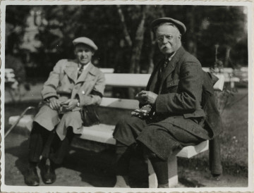 Na zdjęciu znajduje się dwóch mężczyzn siedzacych na ławce w parku.