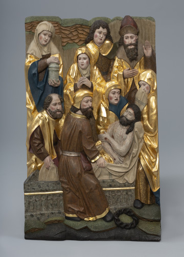 płaskorzeźba ołtarzowa - ujęcie z przodu; Płaskorzeźbiona płyta o kształcie stojącego prostokąta przedstawia grupę postaci stłoczonych przy sarkofagu na tle skalistego pejzażu. Centrum obrazu stanowi ciało Chrystusa składane do sarkofagu ustawionego w poprzek na pierwszym planie. Całun z ciałem dźwigają mężczyźni stojący po lewej stronie - Józef z Arymatei i Nikodem, z których jeden stoi przed grobem i ukazany jest tyłem w trzech czwartych. Tors noszący ślady męki podpiera stojąca po prawej stronie za sarkofagiem matka Ukrzyżowanego, czule obejmując jego głowę. Obok stoi jedna z Marii ocierając chustą zapłakaną twarz. Pozostałe postaci ukazane są z tyłu i powyżej. Sugestywne gesty i spojrzenia budują nastrój żałobnej sceny. Szaty modelowane światłocieniowo są obficie złocone.
