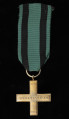 Krzyż Partyzancki - ujęcie z tyłu; Równoramienny, złocony krzyż z ramionami zakończonymi ornamentowym obramowaniem; na rewersie, na ramionach poziomych krzyża napis: PARTYZANTOM, górnym ramieniu data: 1939, na dolnym: 1945. Krzyż zawieszony jest na ciemnozielonej wstążce z czarnymi paskami po bokach. Zawieszenie z tłoczonego z medalem uszka i przewleczonego kółka.