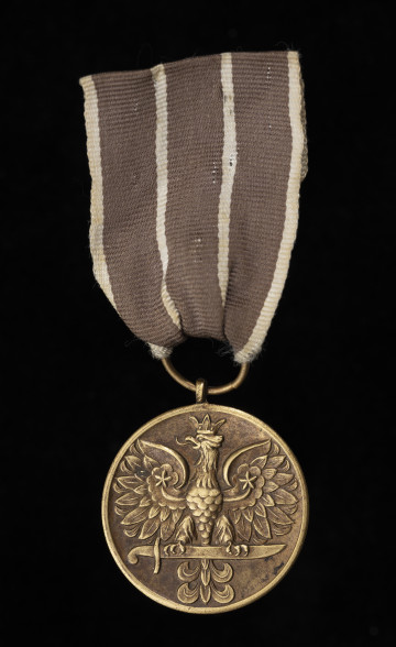 Medal Wojska - ujęcie z przodu; Oznaka medalu okrągła z krawędziami obustronnie płasko podniesionymi. Na awersie znajduje się stylizowany orzeł w koronie, siedzący na mieczu. Wstążka jedwabna, wypłowiała, obecnie w kolorze brązowym (pierwotnie ciemnoczerwona), przedzielona dwoma paskami białymi pośrodku oraz białymi paskami na brzegach.