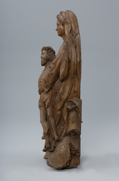 pieta - ujęcie z prawej; Rzeźba o pionowej kompozycji przedstawia dwufigurową grupę: Marię trzymającą martwe ciało Chrystusa. Sylwetka Marii wsparta jest na kamiennym zboczu porośniętym darnią widocznym po bokach i poniżej postaci. Głowę okrywa długi marszczony welon. Obszerny płaszcz nałożony na suknię o długich szerokich rękawach zagina się tworząc głębokie, światłocieniowe fałdowania i szerokie płaszczyzny na krawędziach. Ciało Chrystusa o nieco pomniejszonych proporcjach oddane jest naturalistycznie. Dłońmi podtrzymuje osuwające się diagonalnie martwe ciało Chrystusa o pomniejszonych proporcjach.