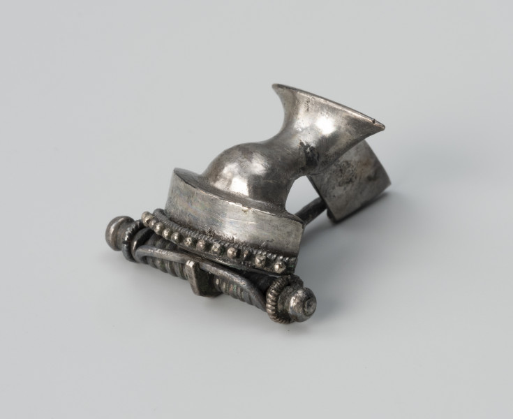Zapinka ze srebra - ujęcie ze skosu z prawej; Srebrna fibula z grzebykiem nad sprężynką zdobionym filigranem.