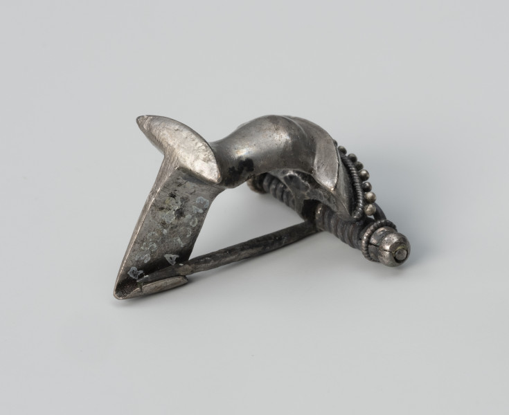 Zapinka ze srebra - ujęcie od tyłu z prawej; Srebrna fibula z grzebykiem nad sprężynką zdobionym filigranem.