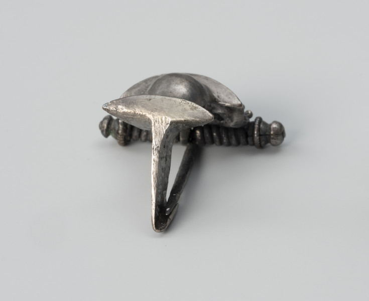 Zapinka ze srebra - ujęcie z tyłu; Srebrna fibula z grzebykiem nad sprężynką zdobionym filigranem.