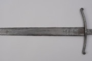 miecz typu XIIIa H2 1b (Oakeshott) - fragment miecza. Z prawej jelec krzyżowy, lekko wygięty ku głowni, z zawiniętymi ku głowicy końcami ramion. Czerwoną farbą na głowni przy nasadzie napis: ODER 1238.