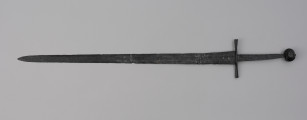 miecz typu XIVa J2 (Oakeschott) - ujęcie z tyłu; Miecz długi półtoraręczny. Głownia długości 95 cm i szer. u nasady 5,6 cm, prosta dwusieczna zbieżna ku sztychowi, łączona wtórnie w dwóch miejscach. Zbrocze długie, sięga 3/4 długości. Pierwotnie po obu stronach głowni znajdował się napis ryty, wypełniony żółtym metalem w postaci krzyżyka oraz trzech liter, z których pierwsza jest nieczytelna, ale przypomina L lub T; druga, środkowa to D; trzecia litera to połączenie I i H. Trzpień rękojeści zwężający się ku końcowi. Jelec krzyżowy o długości 16,7 cm, z rozszerzającymi się ramionami. Głowica kolista, fazowana, dwubocznie spłaszczona o wys. 4,3 cm i szer. 5,6 cm. Powierzchnia z wżerami pokorozyjnymi. Typ wg Oakeschotta: XIVa J2 (ewentualnie XIIIa).