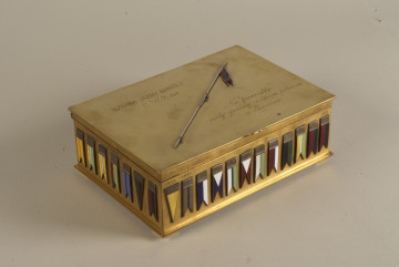 Pamiątkowa kasetka na cygara zdobiona grawerunkami i emaliowanymi proporcami kawaleryjskimi. Wykonana z mosiądzu (złoconego?), w kształcie prostopadłościanu z otwieranym na zawiasach wiekiem