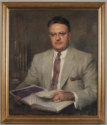 Portret siedzącego mężczyzny w okularach. Mężczyzna ubrany w jasny garnitur, białą koszulę i bordowy krawat. W rękach trzyma książkę z zapisem nutowym. Za prawym ramieniem fragment organów. Obraz sygnowany w prawym dolnym rogu.