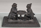 Forma przestrzenna ukazuje dwóch mężczyzn siedzących przy stoliku i grających w karty. Podstawa prostokątna ozdobiona wokół pasem ornamentalnym w motyw roślinny