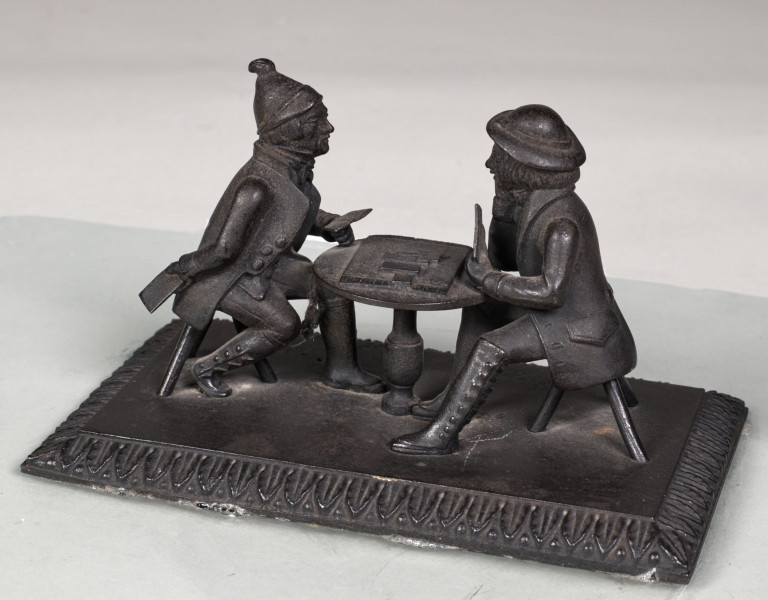 Forma przestrzenna ukazuje dwóch mężczyzn siedzących przy stoliku i grających w karty. Podstawa prostokątna ozdobiona wokół pasem ornamentalnym w motyw roślinny