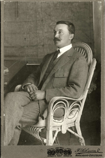 Na zdjęciu znajduje się mężczyzna ubrany w garnitur i białą koszulę z krawatem, siedzący na krześle.