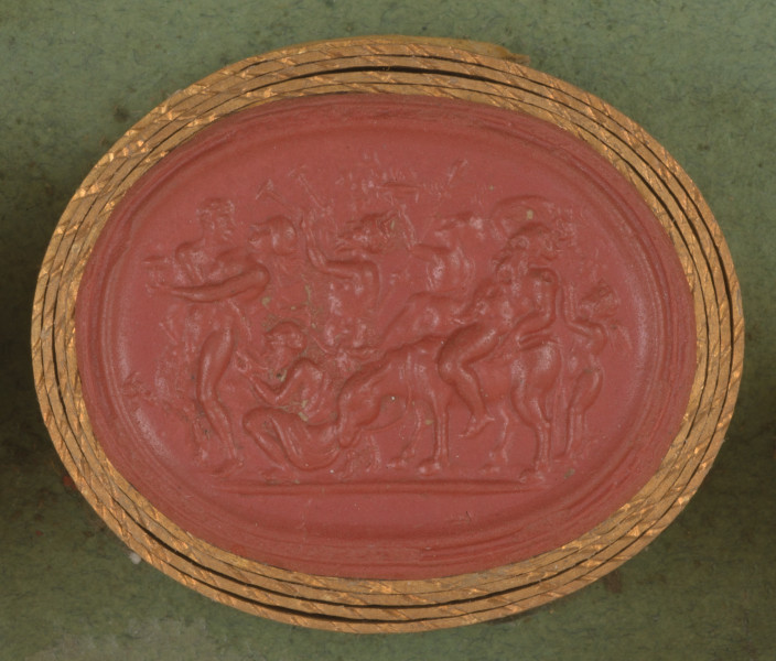 czerwona owalna gemma w grubym złotym obramowaniu; scena wielofiguralna, z lewej strony na przodzie pochodu widoczna naga, omdlewająca kobieta z naczyniem w ręku, trzyma ją w pasie młody Faun z kopytami; za parą kuca postać popijająca wino z naczynia przypominającego kyliks, za nią widoczny jest stary Faun z brodą i różkami na głowie, który gra na dwóch fletach; za nim idzie kobieta niosąca laskę zakończoną szyszką (tyrs) i czarę z ogniem; następnie widoczny jest pulchny, nagi mężczyzna jadący na osiołku, mężczyzna jest brodaty i łysy, jedną rękę trzyma na głowie, drugą trzyma osła; pochód zamyka skrzydlate putto.