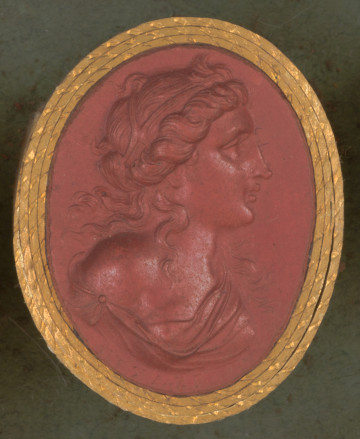 czerwona owalna gemma w grubym złotym obramowaniu; młoda kobieta ukazana z prawego profilu z długimi falowanymi włosami częściowo upiętymi opaską, pojedyncze kosmyki opadają jej na nagie ramiona, poniżej widać fragment luźnej szaty; u dołu sygnatura lliXAEP (PICHLER)