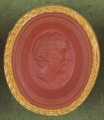 czerwona owalna gemma w grubym złotym obramowaniu; prawy profil starszego mężczyzny z krótkimi włosami i krótką brodą