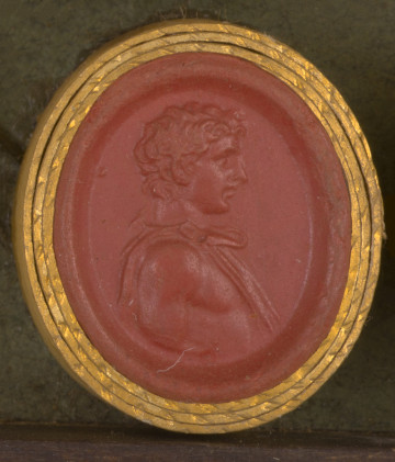 czerwona gemma, owalna pionowa, w grubym złotym obramowaniu. Prawy profil młodego mężczyzny, o krótkich, kręconych włosach. Na gołe ciało narzucony spięty na prawym ramieniu płaszcz.