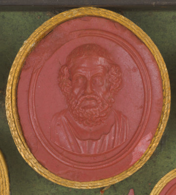 czerwona owalna gemma w grubym złotym obramowaniu; starszy mężczyzna widziany na wprost, ma bujne kręcone włosy, wąsy i brodę, na głowie opaska, w dolnej części widoczna szata