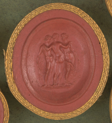 czerwona owalna gemma w grubym złotym obramowaniu; dwie kobiety, stojąc przodem do widza, trzymają w rękach szal. Naga kobieta w środku jest odwrócona tyłem i obejmuje pozostałe kobiety ramionami.