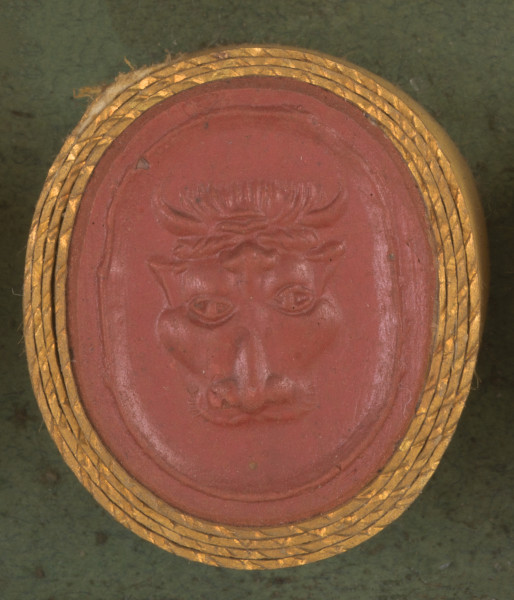 czerwona owalna gemma w grubym złotym obramowaniu; maska głowy byka widziana z przodu; byk na głowie ma opaskę