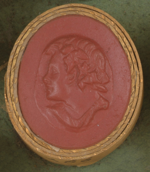 czerwona owalna gemma w grubym złotym obramowaniu; głowa młodego Fauna widoczna z lewego profilu, z wieńcem z winorośli na głowie, poniżej widoczna część szaty