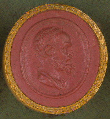 czerwona owalna gemma w grubym złotym obramowaniu; prawy profil starszego mężczyzny z krótkimi lekko falującymi włosami, wydatnym czołem, wąsami i falowaną brodą, poniżej widoczny fragment tuniki