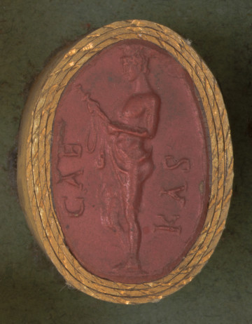 czerwona owalna gemma w grubym złotym obramowaniu; młody mężczyzna widoczny z lewego boku, o nagim torsie i pasie przykrytym płaszczem przewieszonym przez prawe ramię; ma krótkie kręcone włosy i lekko opuszczoną głowę,patrzy na miecz trzymany w rękach. Przed postacią i za nią w otoku napis CAE (po lewej) KAS (po prawej) (CAECAS)