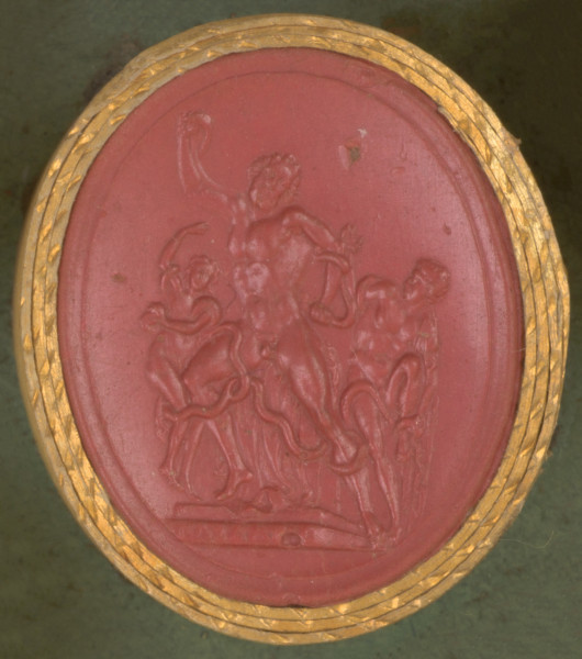 czerwona owalna gemma w grubym złotym obramowaniu, scena przedstawiająca 3 postacie: dojrzałego mężczyznę w centrum oraz dwóch młodzieńców po obu jego bokach, walczących z oplatającym ich ciała wężem. 