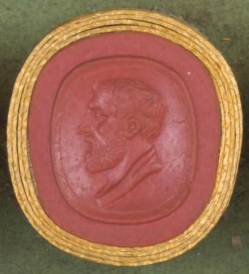 czerwona owalna gemma w grubym złotym obramowaniu; lewy profil starszego mężczyzny, z krótkimi włosami, wąsami i krótką brodą, pod szyją widoczny fragment szaty