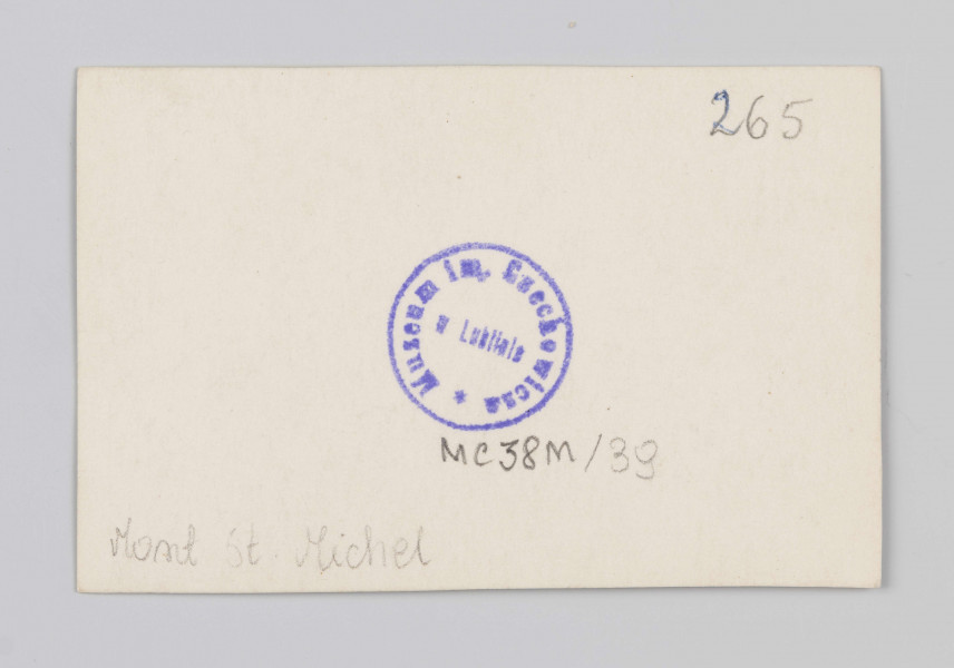 MC/M/38/39/ML - Fotografia w pozycji poziomej. Na zdjęciu przedstawiono widok na ścianę zachodnią refektarza. Centrum przedstawienia stanowią drzwi prowadzące na wirydaż oraz znajdujące się nad nimi okno maswerkowe. Sala refektarza z obu stron jest symetrycznie zdobiona arkadami z przyściennymi służkami z głowicami poączkowymi. Pomiędzy każdym przeżsłem znajduje się wsmukłe wąskie okno. Sala sklepiona półkoliście.
Na odwrocie w prawym górnym rogu napis ołówkiem: 