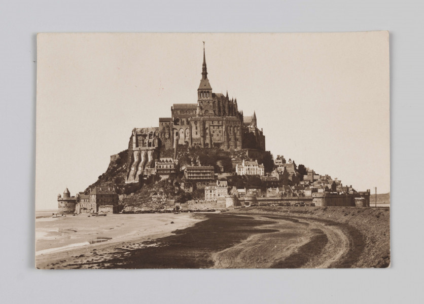 MC/M/38/43/ML - Fotografia w pozycji poziomej. Na zdjęciu uwieczniono widok ogólny na górę Mont Saint-Michel z górującym nad nią opactwem. Po prawej znajduje się ziemna grobla łącząca wyspę z kontynentem, po lewej wody rzeki Couesnon.
Na odwrocie w prawym górnym rogu napis ołówkiem: 