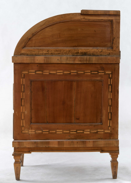 Biurko przyścienne na sześciu nóżkach graniastych zbieżnych. W części dolnej prostokątny prześwit zamknięty tylną ścianą. Po jego bokach po dwie szuflady, powyżej jeszcze trzy. Część górna ćwierćcylindryczna zamykana żaluzją chowaną pod górna płytą powyżej pięciu szufladek, boki zdobione plastycznym ornamentem cekinowym. Lico pokryte fornirem z intarsją ramkową i wzorem arkadkowym. Blat wyłożony skórą cielęcą. Uchwyty szuflad zewnętrznych i żaluzji to nałożone okucia okrągłe z tarczą, szufladki w części górnej mają uchwyty okrągłe z gładką główką.  