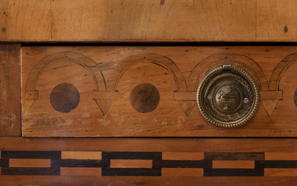 Biurko przyścienne na sześciu nóżkach graniastych zbieżnych. W części dolnej prostokątny prześwit zamknięty tylną ścianą. Po jego bokach po dwie szuflady, powyżej jeszcze trzy. Część górna ćwierćcylindryczna zamykana żaluzją chowaną pod górna płytą powyżej pięciu szufladek, boki zdobione plastycznym ornamentem cekinowym. Lico pokryte fornirem z intarsją ramkową i wzorem arkadkowym. Blat wyłożony skórą cielęcą. Uchwyty szuflad zewnętrznych i żaluzji to nałożone okucia okrągłe z tarczą, szufladki w części górnej mają uchwyty okrągłe z gładką główką.  