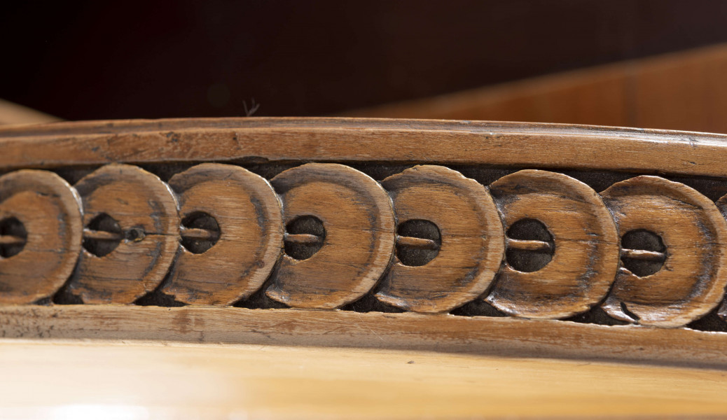 Biurko przyścienne na sześciu nóżkach graniastych zbieżnych. W części dolnej prostokątny prześwit zamknięty tylną ścianą. Po jego bokach po dwie szuflady, powyżej jeszcze trzy. Część górna ćwierćcylindryczna zamykana żaluzją chowaną pod górna płytą powyżej pięciu szufladek, boki zdobione plastycznym ornamentem cekinowym. Lico pokryte fornirem z intarsją ramkową i wzorem arkadkowym. Blat wyłożony skórą cielęcą. Uchwyty szuflad zewnętrznych i żaluzji to nałożone okucia okrągłe z tarczą, szufladki w części górnej mają uchwyty okrągłe z gładką główką.  