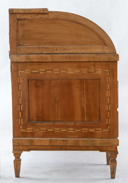 Biurko przyścienne na sześciu nóżkach graniastych zbieżnych. W części dolnej prostokątny prześwit zamknięty tylną ścianą. Po jego bokach po dwie szuflady, powyżej jeszcze trzy. Część górna ćwierćcylindryczna zamykana żaluzją chowaną pod górna płytą powyżej pięciu szufladek, boki zdobione plastycznym ornamentem cekinowym. Lico pokryte fornirem z intarsją ramkową i wzorem arkadkowym. Blat wyłożony skórą cielęcą. Uchwyty szuflad zewnętrznych i żaluzji to nałożone okucia okrągłe z tarczą, szufladki w części górnej mają uchwyty okrągłe z gładką główką.  