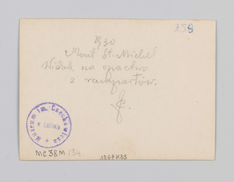 MC/M/38/34/ML - Fotografia w pozycji wertyalnej. Linia horyzontu dzieli zdjęcie na mniej więcej połowę. Centrum obrazu przesunięte nieco na lewą stronę. Opactwo wraz z przylegającymi budynkami kompozycyjnie wpisane w trójkąt. Światło rozproszone, jego źródło znajduje się poza fotografią z lewej strony.
Na zdjęciu ukazano zabudowania Mont Saint-Michel od strony wschodniej. Na pierwszym planie, poniżej linii horyzontu znajdują się zabudowania wioski. Powyżej linii horyzontu znajduje się opactwo wraz z blankami - po prawej stronie tak zawany La Merveille z refektarzem, po lewej zaś absyda katedry z iglicą zbudowaną na przecięciu naw.
Na odwrocie (ustawienie w pozycji horyzontalnej) w prawym górnym rogu napisana niebieskim długopisem liczba 