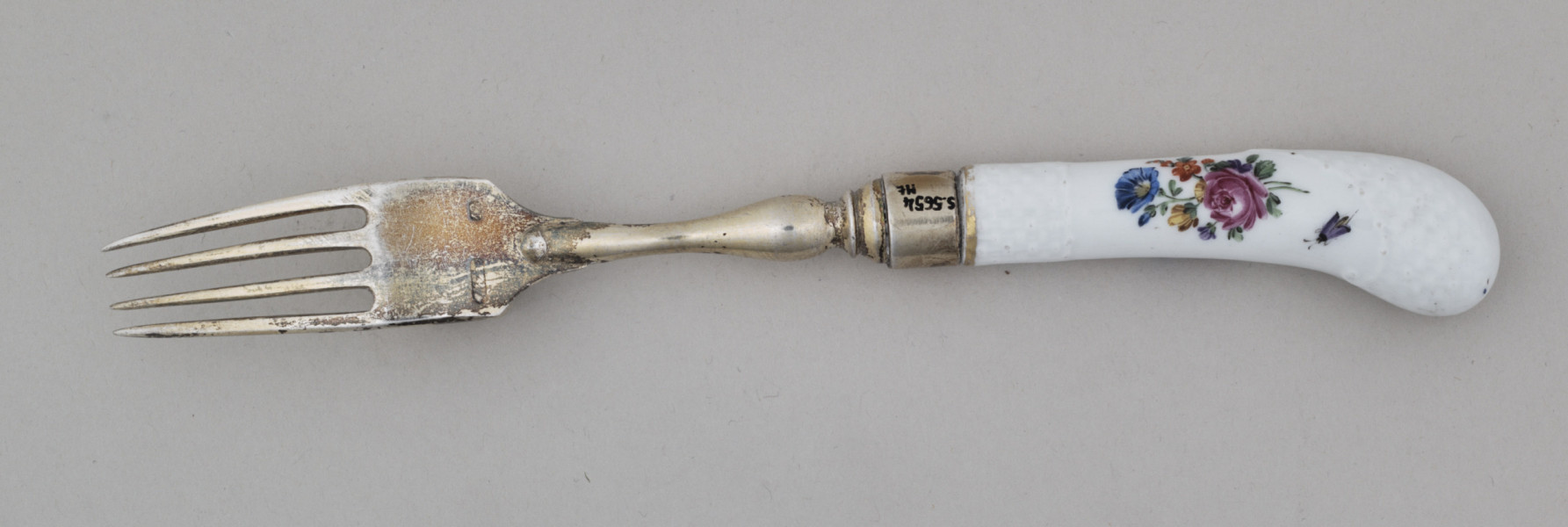 Widelec śniadaniowy, czterozębny. Zęby wygięte, zwężające się przy zakończeniu. Trzonek z nakładką ze srebra złoconego z białej porcelany